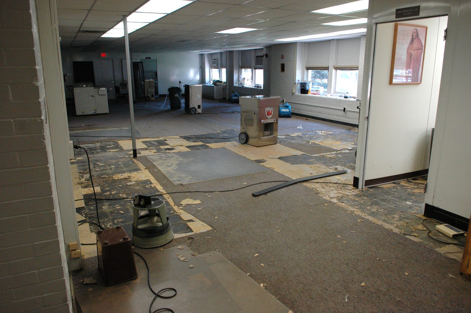 Air mover and dehumidifier running on the stripped floor of a flooded room, carpet pulled back to the slab