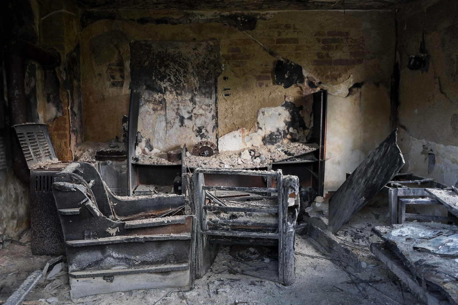 Burned-out living room with charred furniture, soot on every wall and ash on the floor